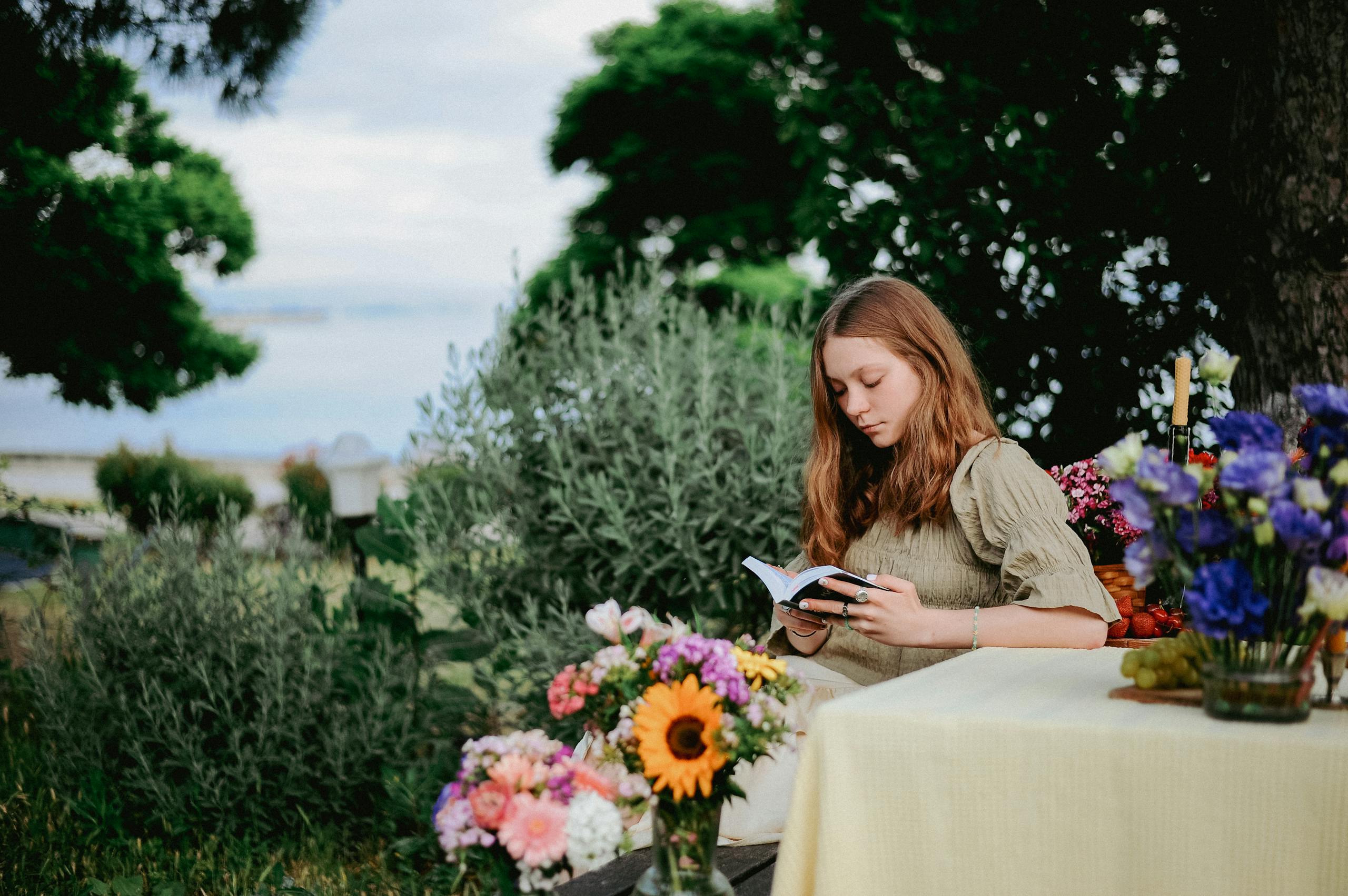 Pretty Girl Relaxing at a Picnic Table with a Book in Hands